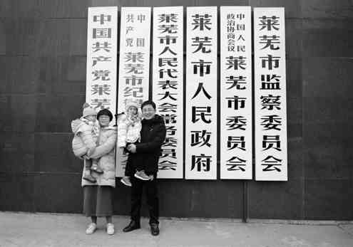 ▲市民邹忠玉、王雪夫妇抱着两个孩子在原莱芜市政府门前拍照留念。